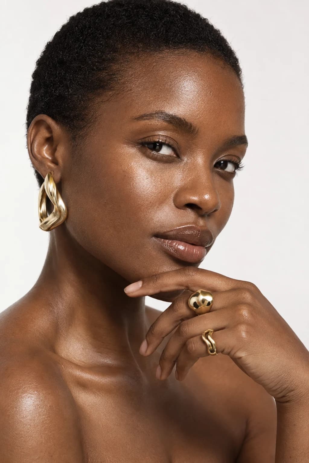 Model wearing a sculptural gold earring and two gold rings
