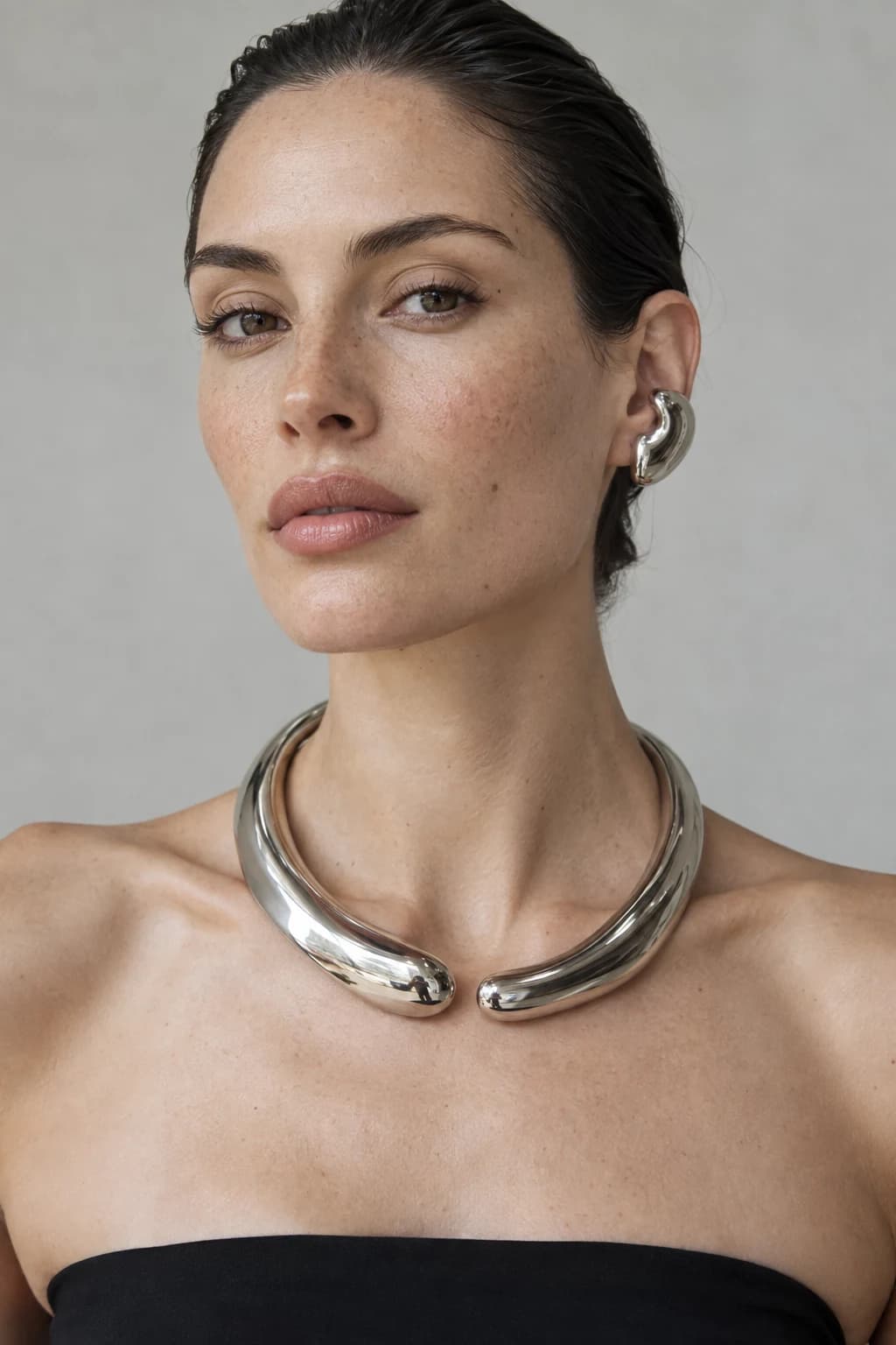 Model wearing a sculptural silver necklace and earring in an editorial portrait