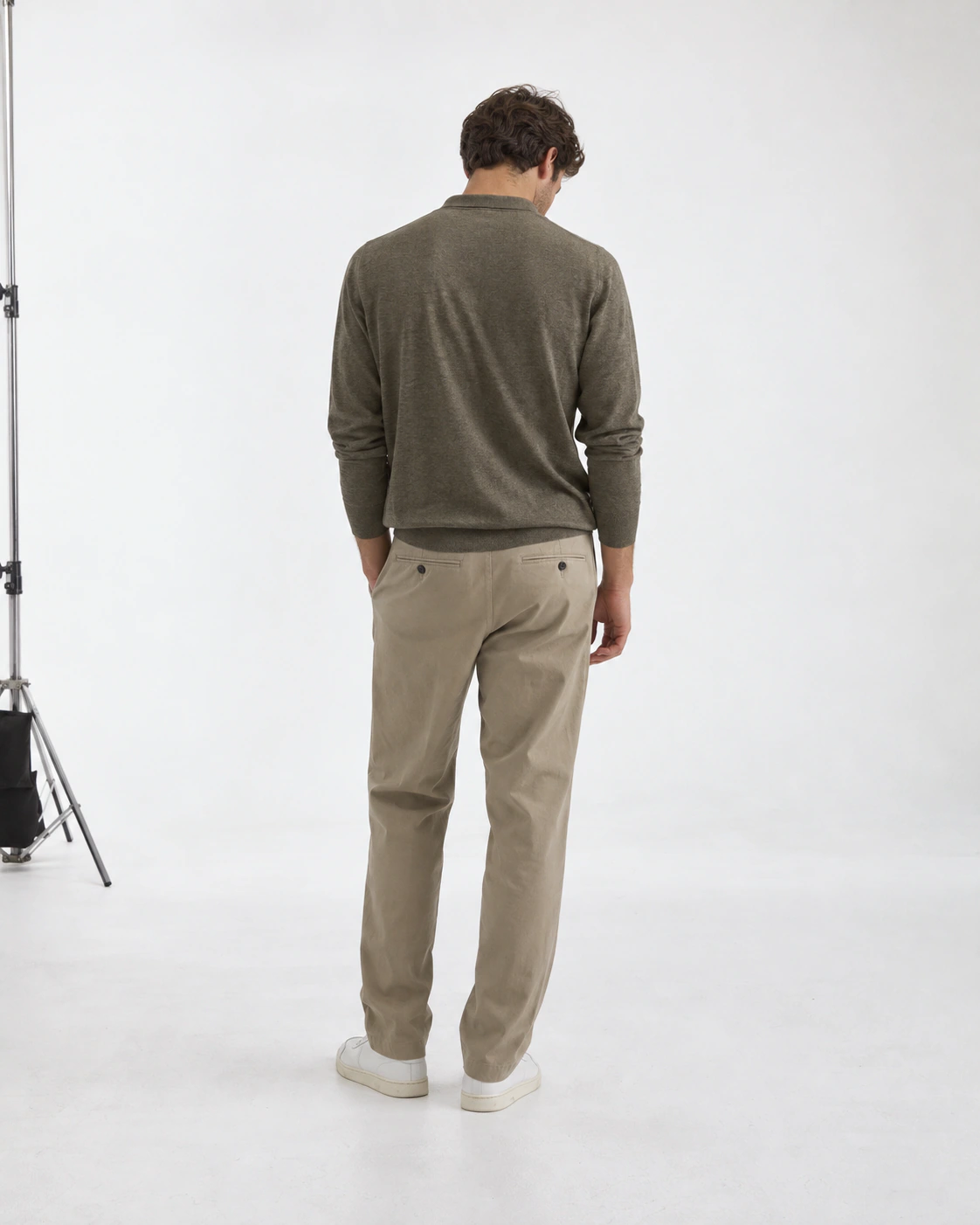 Male model seen from behind in a long-sleeve polo and chinos inside a white studio
